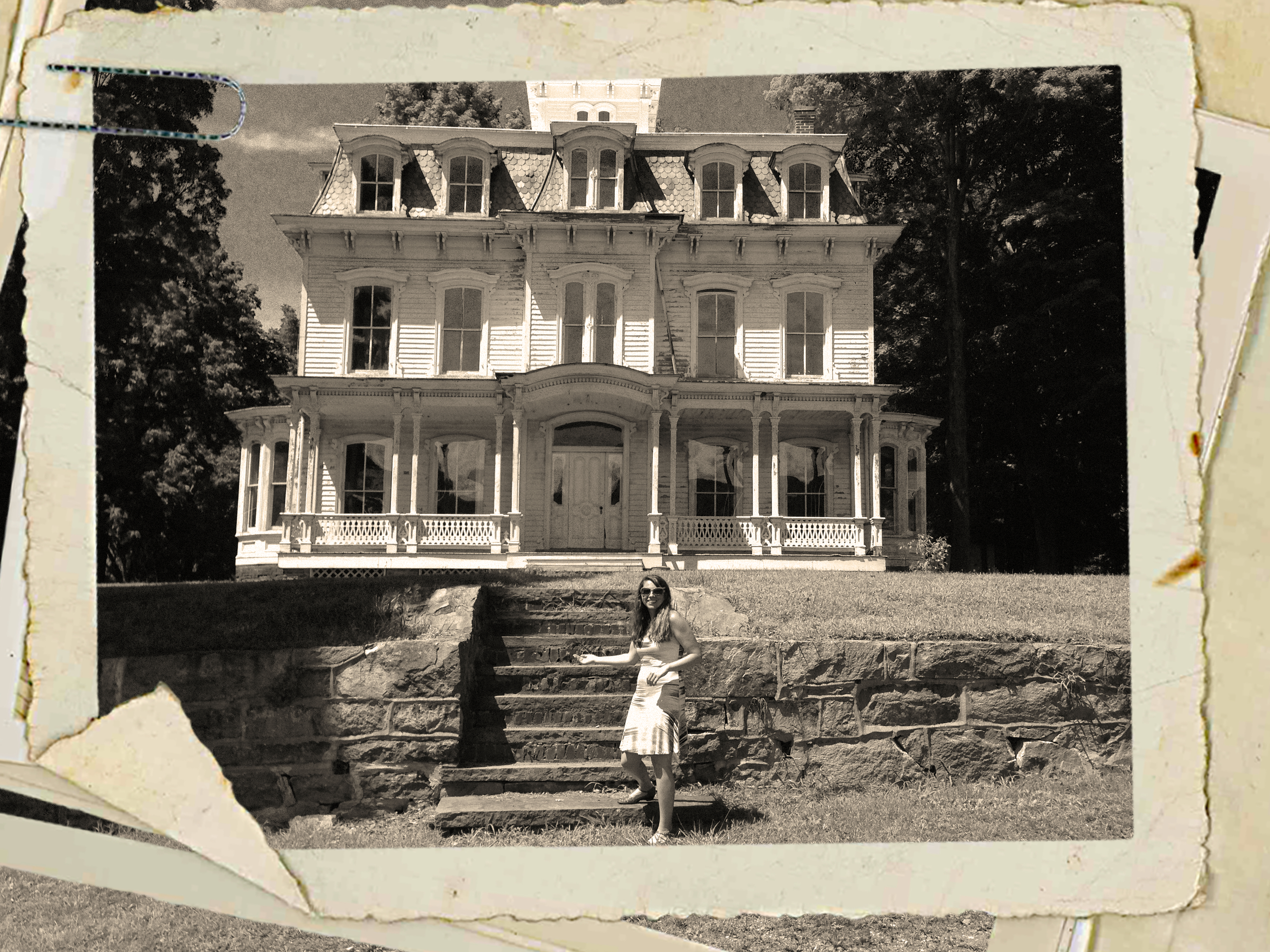 Black and white photo of a smiling woman in front of an old Victorian house.