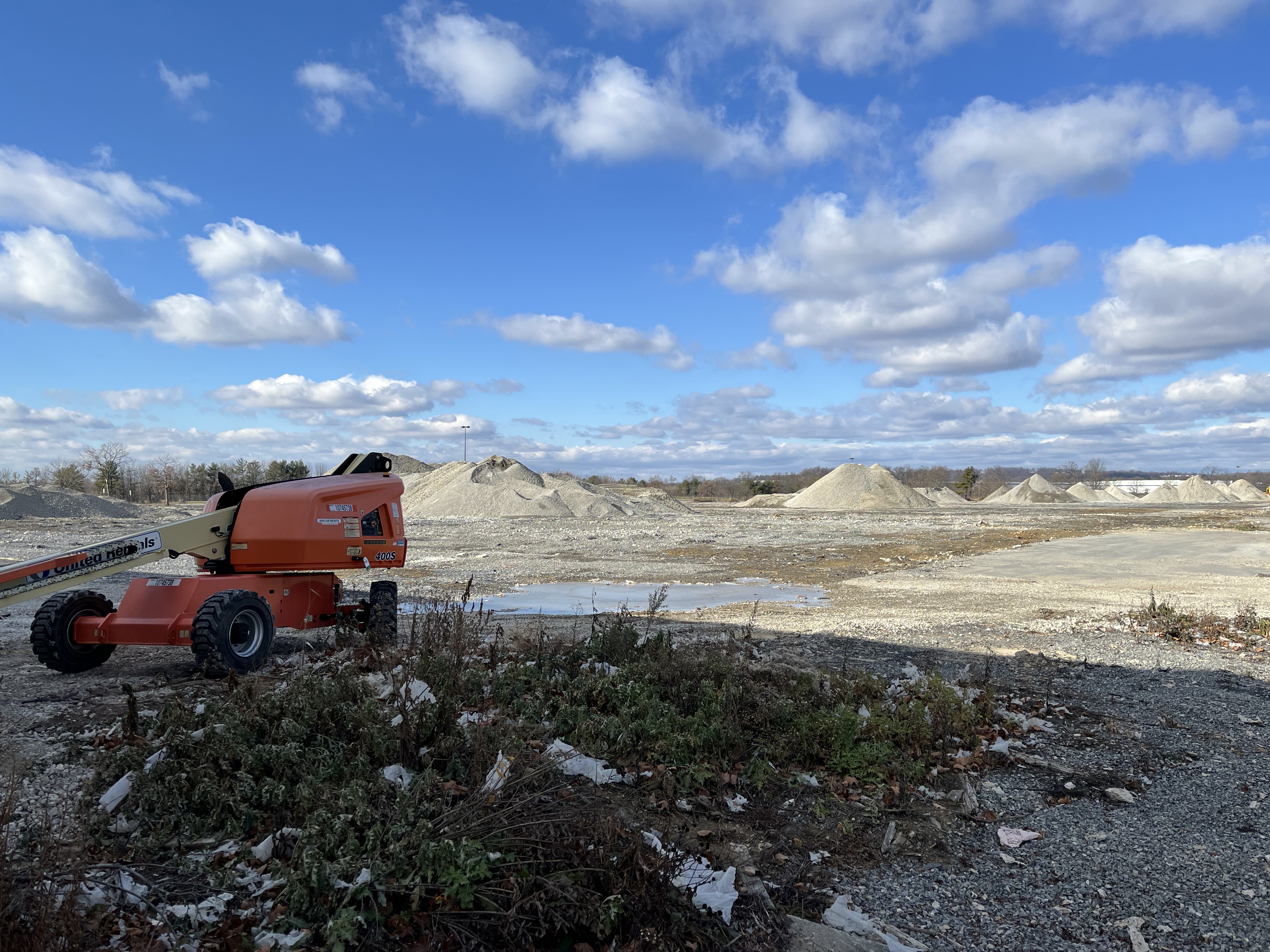 Piles of rubble and a construction vehicle against a cloud-filled blue sky.