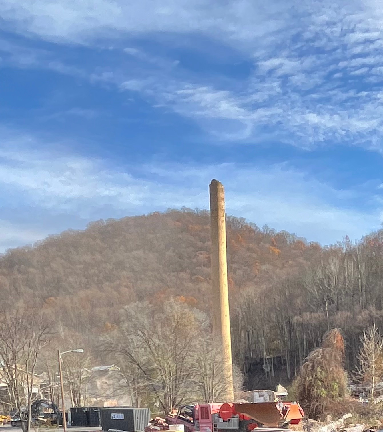 Photo of a factor smokestack against a bright blue sky with various construction equipment at the base.