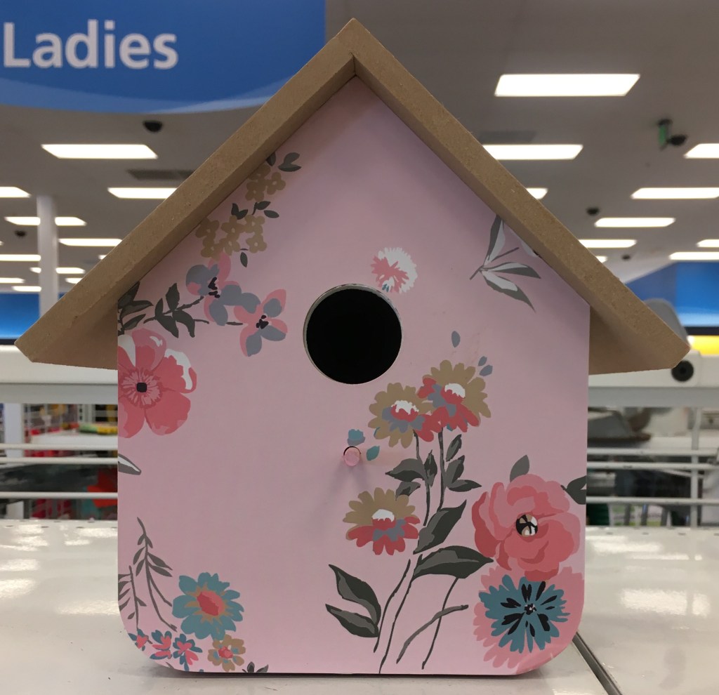 Photo of a pink painted birdhouse with flower illustrations on a shelf in a store.
