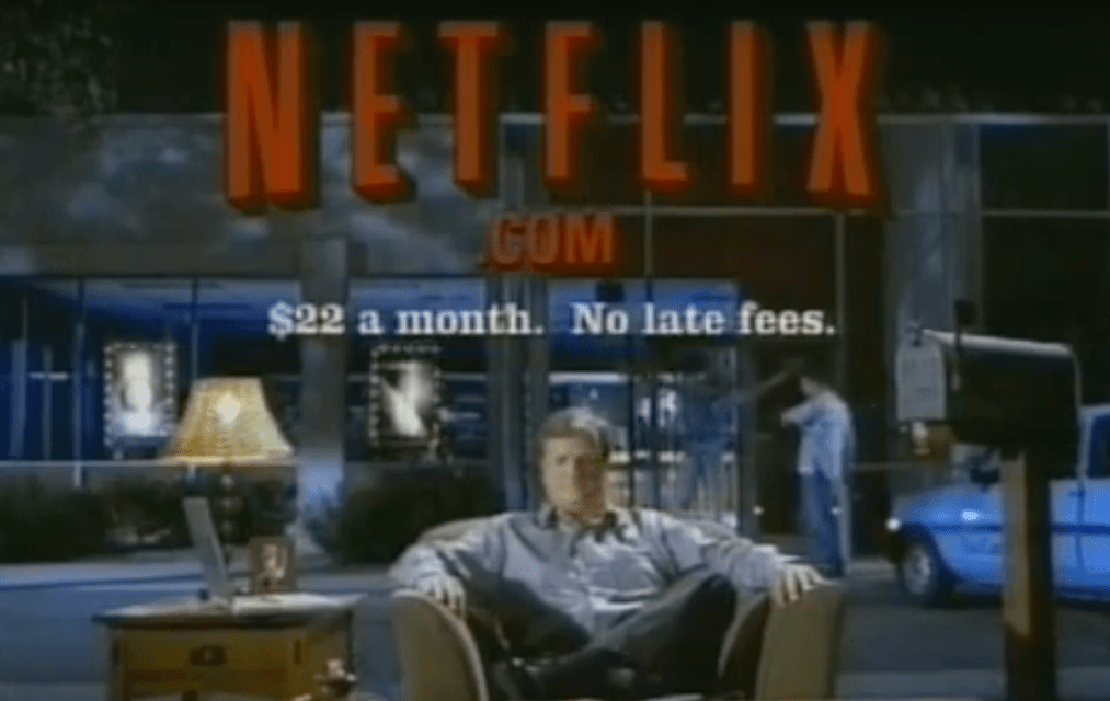 Screenshot of a vintage Netflix TV commercial with a man sitting in an armchair beside a mailbox and the text at the top: Netflix.com. $22 a month. Not late fees.