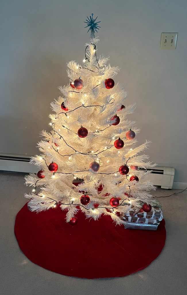 Photo of a small white Christmas tree with red and pink ornaments and a blue star on top.