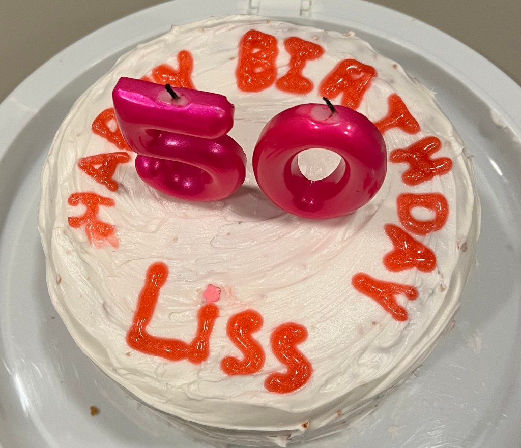 Photo of a birthday cake with hot pink "50" shaped candles and icing that reads "Happy Birthday Liss"