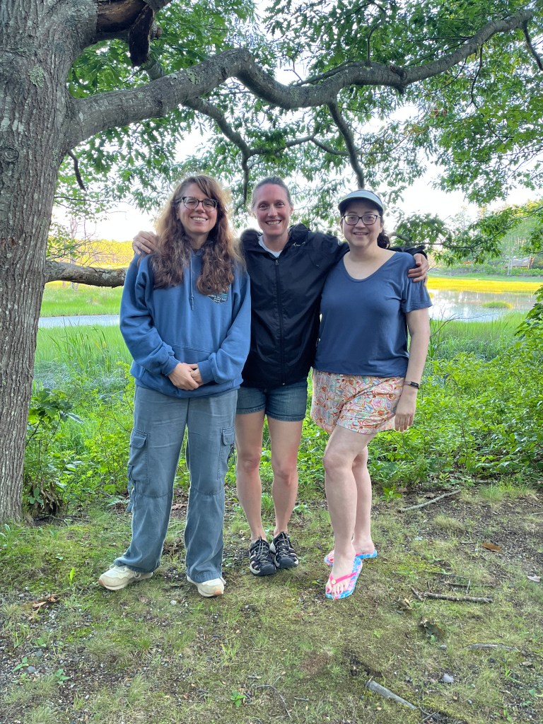 Photo of three middle-aged women standing in front of a salt marsh.
