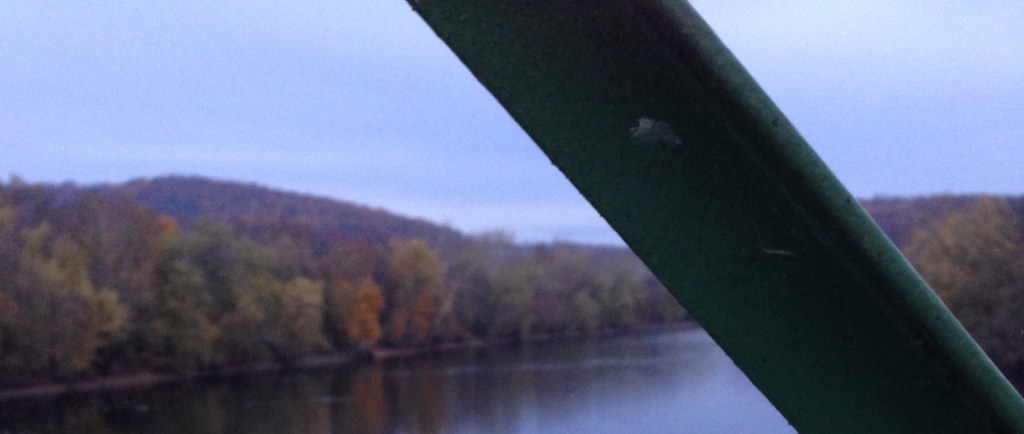 Photo of a river taken from a bridge with trees in autumn colors and hills.